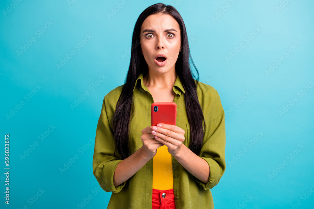 Photo of shocked young girl hold mobile phone open mouth staring camera wear green shirt isolated blue color background Photo of shocked young girl hold mobile phone open mouth staring camera wear green shirt isolated blue color background