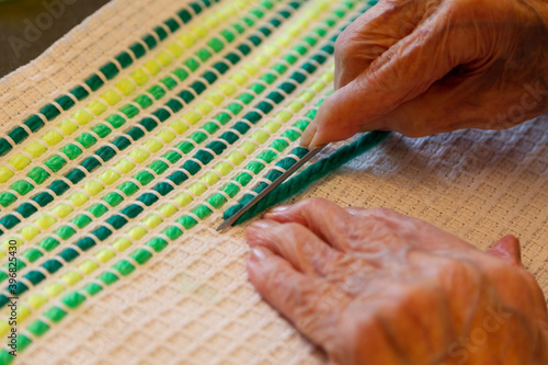 Aged hands working on embroidery with green thread on fabric