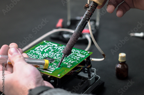 Technician repair electronic circuit board with soldering iron and tin wire. Repair of electronic devices, tin soldering parts