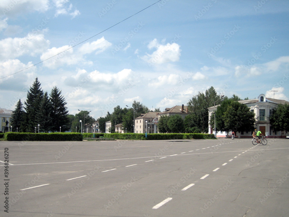 A wide, deserted square in a small provincial city in Russia. Gray asphalt surrounded by several two-storey houses in the centre of the city.