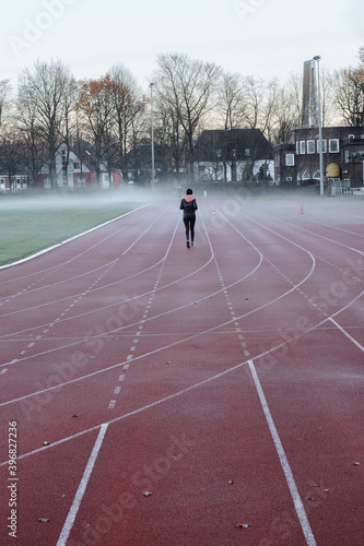 Woman makes a run at the stadium in the fog, rear view from afar