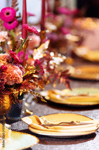 Elegant table set with glasses decorated in gold  lighted candles and rose flowers. Selected focus and blurred background