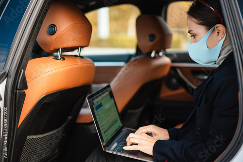 Focused businesswoman wearing face mask working with laptop in car