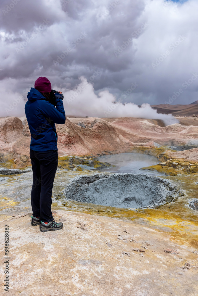 Woman with a camera photographing some mud pits with volcanic activity in the Andean Highlands, Bolivia.