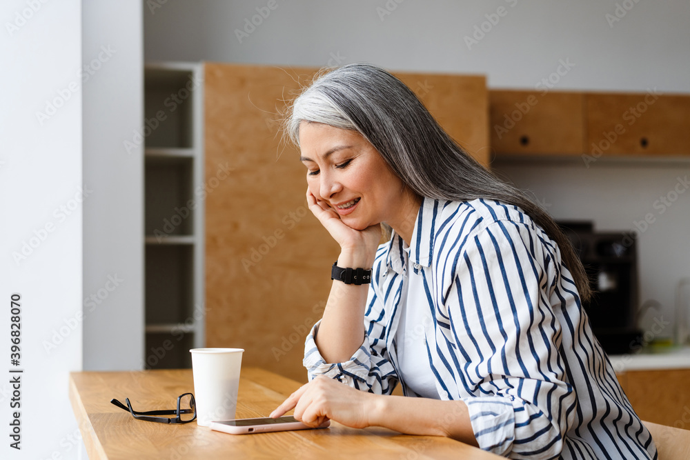 Happy white-haired mature woman drinking coffee and using mobile phone Happy white-haired mature woman drinking coffee and using mobile phone