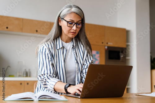 Serious mature woman working with laptop while sitting at table