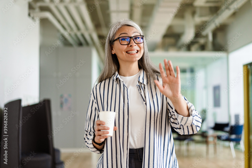 Happy white-haired mature woman waving hand while drinking coffee Happy white-haired mature woman waving hand while drinking coffee