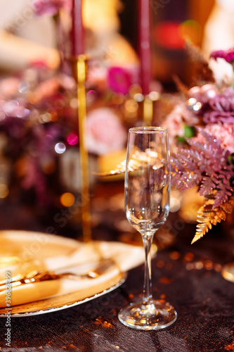 Table served for Christmas dinner, festive setting with decorations, burning candles and golden fern branches, glasses. Selected focus and blurred background