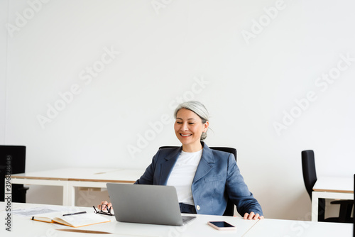 Cheerful white-haired businesswoman smiling while working with laptop