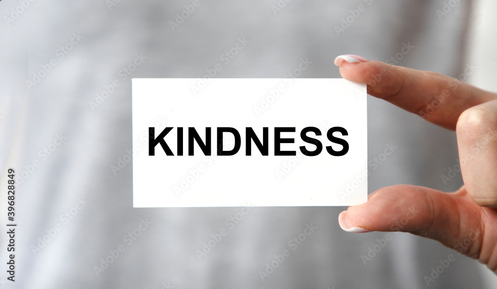 The girl in front of her holds a business card with the text KINDNESS, next to a pen and reports. The girl in front of her holds a business card with the text KINDNESS, next to a pen and reports.