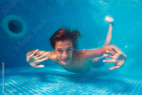 Happy handsome boy float underwater with smiling portrait in the pool showing palms and smile photo