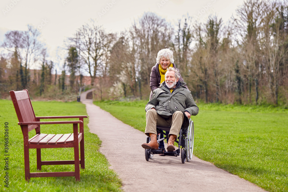 Senior Woman Pushing Senior Man In Wheelchair Outdoors In Fall Or Winter Park Senior Woman Pushing Senior Man In Wheelchair Outdoors In Fall Or Winter Park