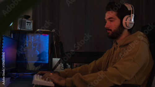 Male using PC and concentrating while wearing white headphones in a darkened room
