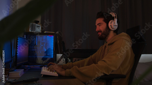 Male using PC and concentrating while wearing white headphones in a darkened room