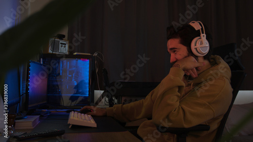 Male using PC and concentrating while wearing white headphones in a darkened room