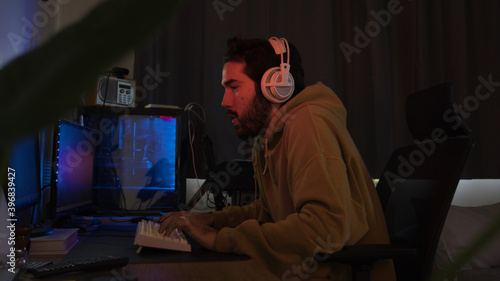 Male using PC and concentrating while wearing white headphones in a darkened room