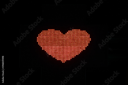 Glowing pixel red heart of LED lamps on black background. Red heart symbol of romance, love, health, medicine, self-care Stock photo with empty space for text and design
