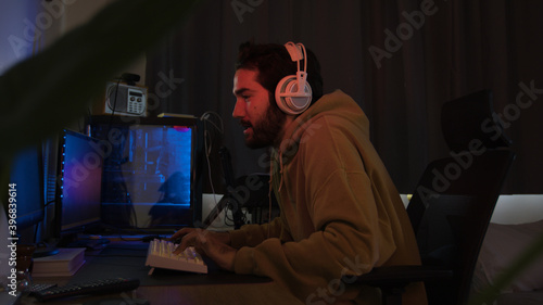 Male using PC and concentrating while wearing white headphones in a darkened room