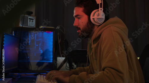 Male using PC and concentrating while wearing white headphones in a darkened room