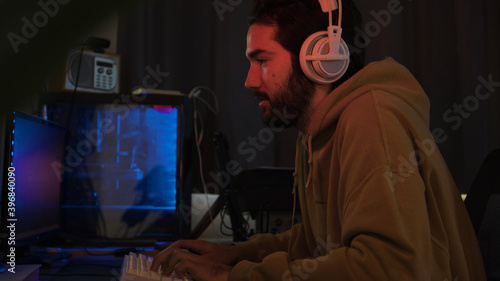 Male using PC and concentraiting while wearing white headphones in a darkened room