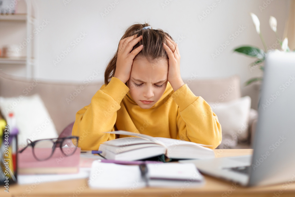 Exhausted schooler girl suffering from doing homework, tired from studying at home, getting ready before exams, stressed with difficult task, reading book, using laptop. Home education, homeschooling Exhausted schooler girl suffering from doing homework, tired from studying at home, getting ready before exams, stressed with difficult task, reading book, using laptop. Home education, homeschooling