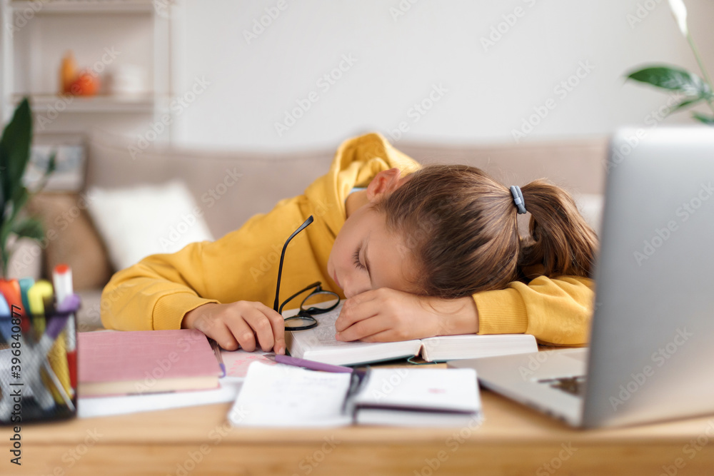 Exhausted school girl sleeping at desk while doing lots of homework, getting ready before exams, stressed, got tired from studying, too much learning. Home interior. Homeschooling, distance education Exhausted school girl sleeping at desk while doing lots of homework, getting ready before exams, stressed, got tired from studying, too much learning. Home interior. Homeschooling, distance education