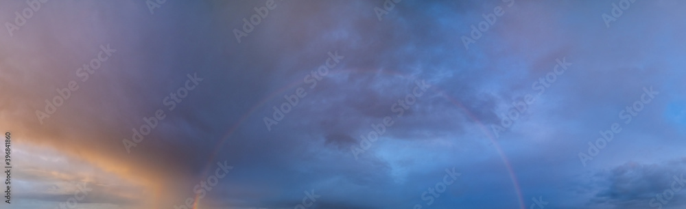 Summer sunset after rain sky panorama with fleece purple clouds and rainbow. Evening dusk good weather natural cloudscape background.