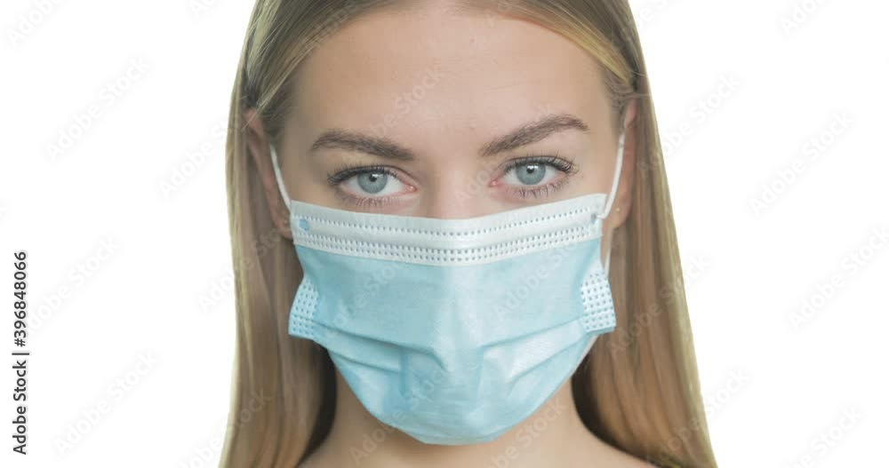 A young blonde woman wearing a surgical mask turns to look at the camera. A young blonde woman wearing a surgical mask turns to look at the camera.