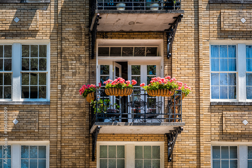 Savannah, Georgia apartment building window balcony open doors during sunny day in summer with old historic brick architecture and flowers in garden - obrazy, fototapety, plakaty 