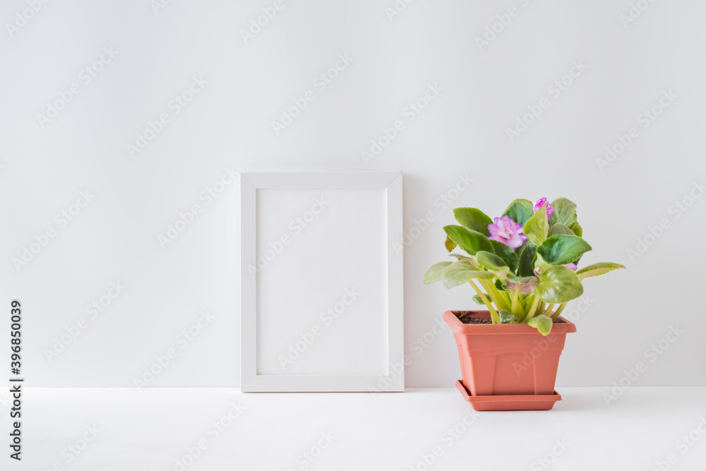 Mockup with a white frame, flowers in a pot on a light background Mockup with a white frame, flowers in a pot on a light background