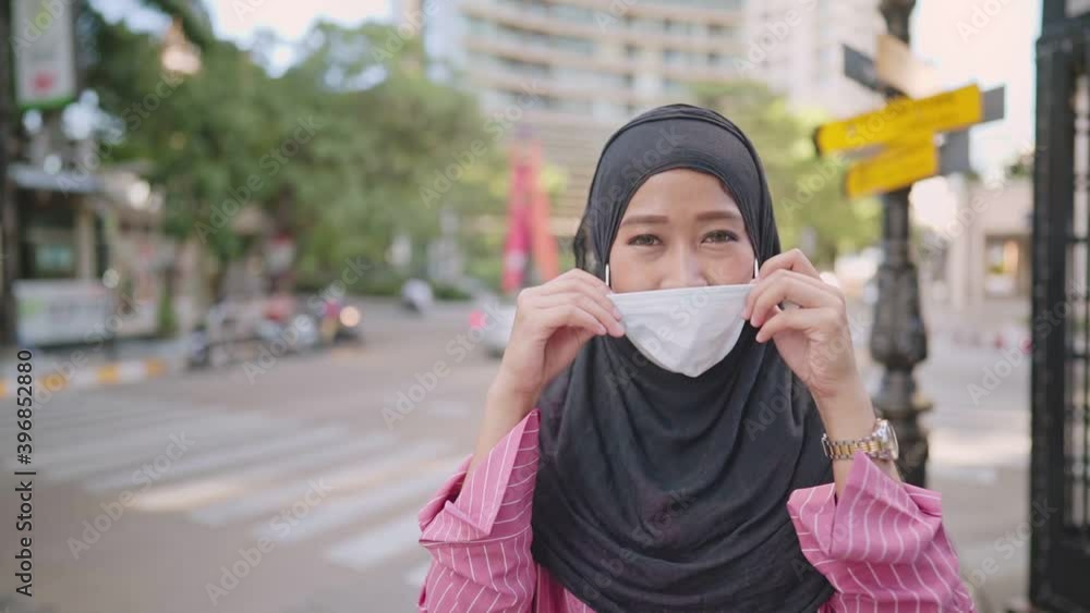 Slow motion shot of Young Asian Muslim woman put on medical face mask. standing on the street side ,city urban new normal, feel confident thumb up, COVID-19 pandemic, infectious disease protection Slow motion shot of Young Asian Muslim woman put on medical face mask. standing on the street side ,city urban new normal, feel confident thumb up, COVID-19 pandemic, infectious disease protection