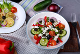 White plate with grilled zucchini on lettuce leaves and Greek salad on a gray table on a napkin with a fork near vegetables.