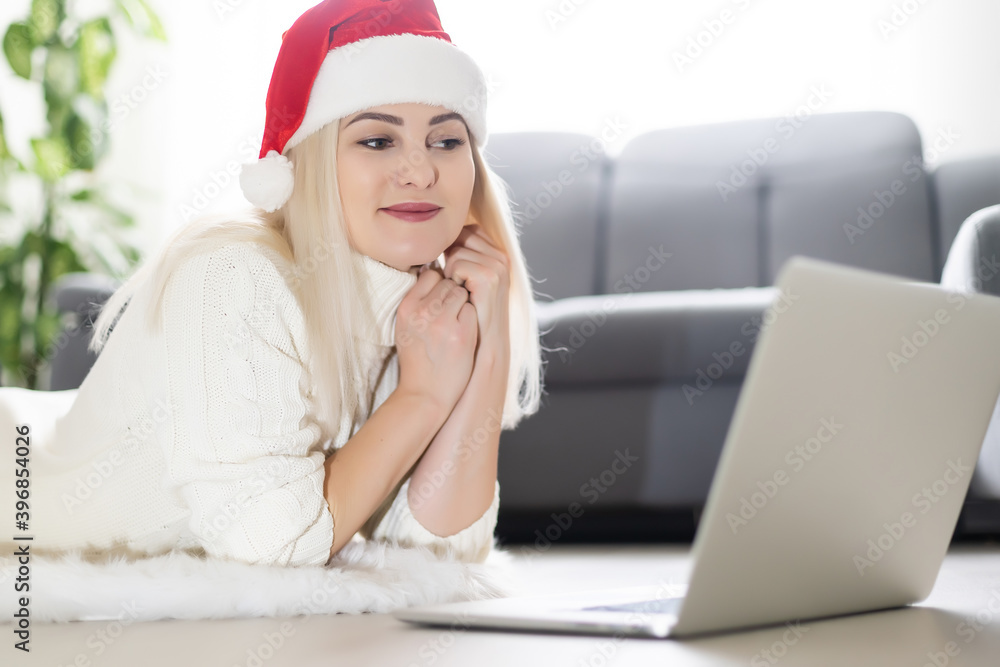 Happy young woman browsing the internet over the christmas holiday season as she sits on the floor in the living room in front of a decorated Xmas Happy young woman browsing the internet over the christmas holiday season as she sits on the floor in the living room in front of a decorated Xmas