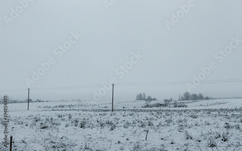 Country side meadow field covered with snow, first winter snow, frozen ground, grey color sky