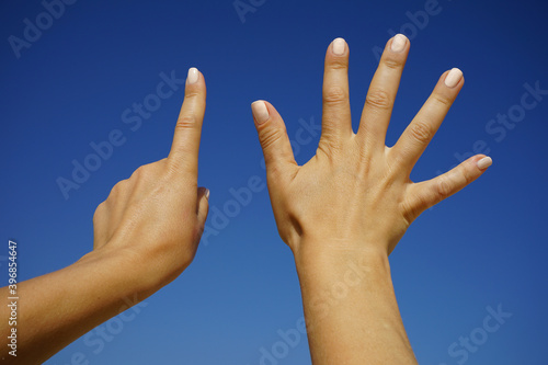 women's hands show the number six against a cloudless blue sky