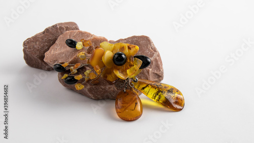 Beautiful yellow vintage Baltic amber brooch in the form of a flower on the natural pink stone. Isolated jewelry made of amber and black agate on the white background.