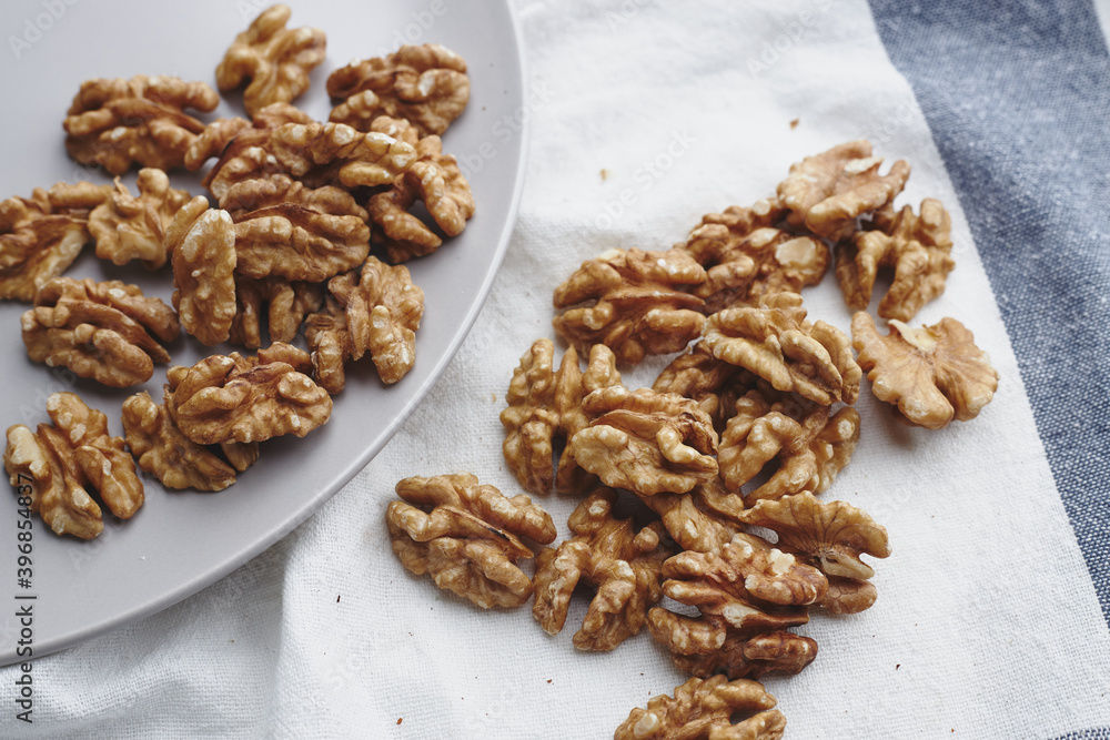 walnut kernels on a white blue tablecloth, craft paper and a gray round plate. ripe walnut fruit for vegenans walnut kernels on a white blue tablecloth, craft paper and a gray round plate. ripe walnut fruit for vegenans