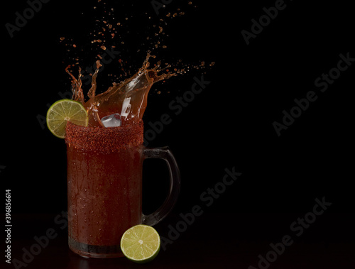 Refreshing drink made with beer, lemon, hot sauce and spicy powder with ice in a big jar
