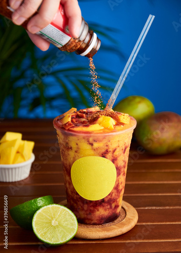Woman hand pouring spicy powder to cold mango smoothie