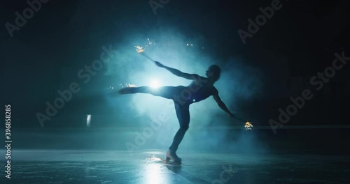 Cinematic shot of young female figure skater is performing a woman's single skating choreography with sparklers on ice rink during a competition. Concept of celebration, holidays, victory