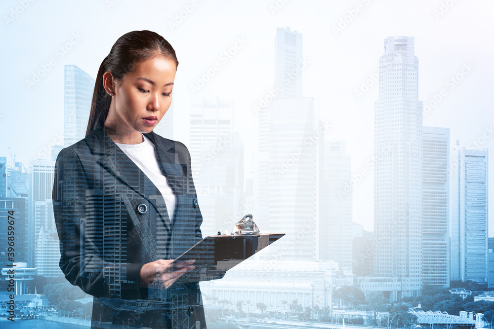 Attractive young Asian business woman in suit taking notes into the notebook, new career opportunities, MBA assignment. Singapore on background. Double exposure. Attractive young Asian business woman in suit taking notes into the notebook, new career opportunities, MBA assignment. Singapore on background. Double exposure.