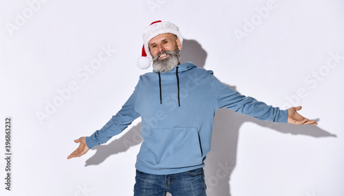 elderly successful man with a beard wearing a Santa Claus hat spread his arms out for hugs, just for the holidays, he is in a blue sweater with a hood on a white background