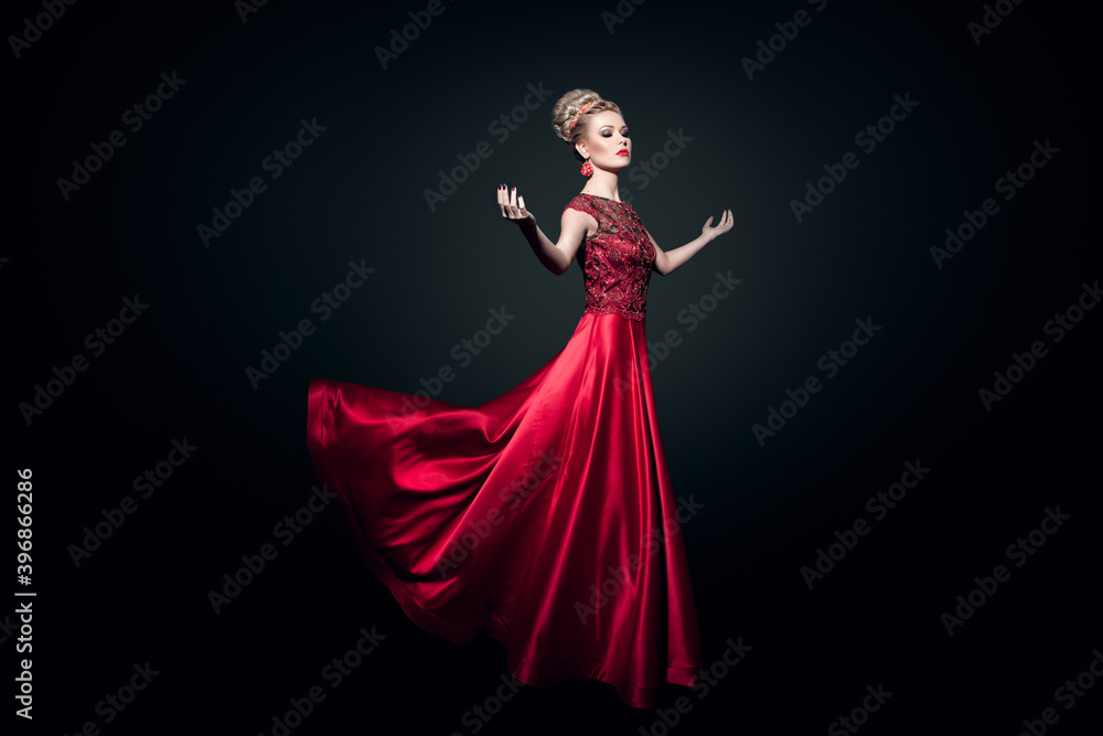 Fototapeta premium Fulll length view of a wonderful young woman dressd in a long fluing red dress with raised hands, over black background.