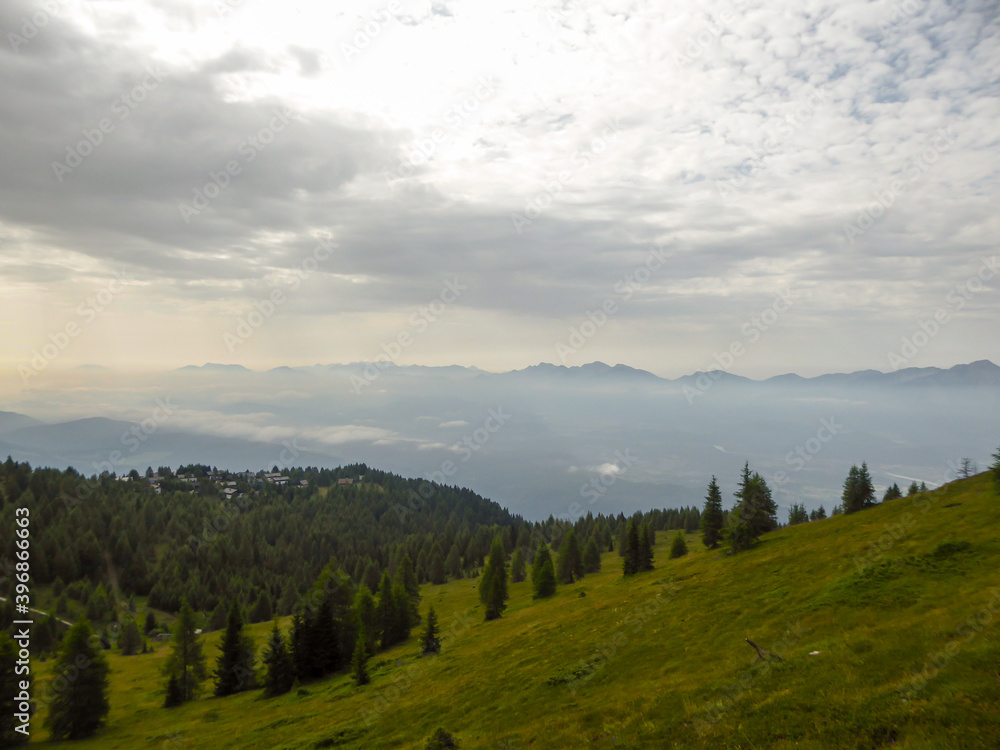 A panoramic view of the slopes of Gerlitzen in Austria. The valley below is shrouded with fog, high peaks popping out above the fog level. Lush green Alpine slopes. Serenity and calmness