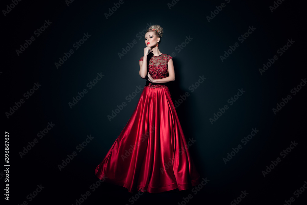 Fototapeta premium Fulll length image of a beautiful girl dressd in a long fluing red dress, over black background.