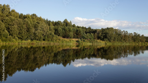 Beautiful Volga river shore with green forest on blue sky with white clouds background, reflection in calm water in perspective at summer day, scenery Russian natural landscape view from water