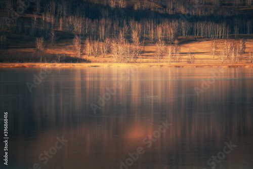 Yellow autumn forest with reflections in the ice surface of the frozen lake. Beautiful autumn landscape.
