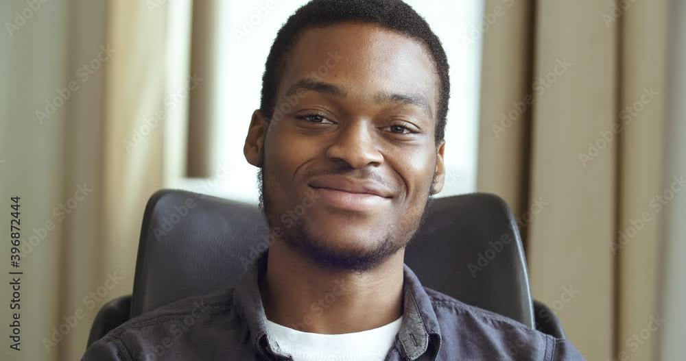 Front closeup portrait of young mixed race handsome African American black business man afro student sitting in home office looking friendly at camera. Human black male face, toothy smile concept Front closeup portrait of young mixed race handsome African American black business man afro student sitting in home office looking friendly at camera. Human black male face, toothy smile concept