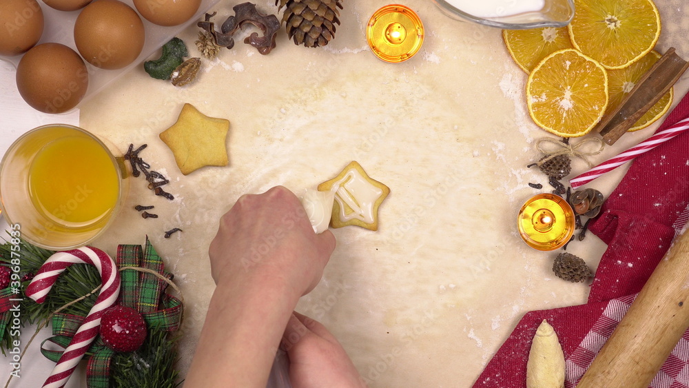 A young woman decorates festive Christmas cookies with colored star icing. View from above. A young woman decorates festive Christmas cookies with colored star icing. View from above.