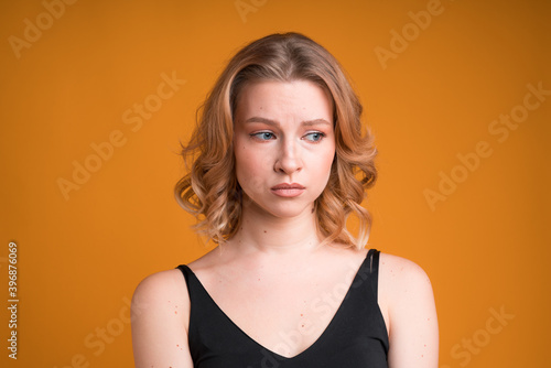 A portrait of a moody Caucasian girl isolated on orange background. She's dissapointed and sad, looking sideways and pouting lips photo